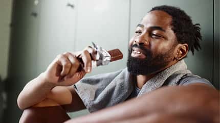 Glücklicher Sportler isst Proteinriegel in der Umkleidekabine des Fitnessstudios Glücklicher Sportler isst Proteinriegel in der Umkleidekabine des Fitnessstudios