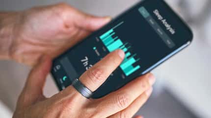 Closeup einer Hand mit Fitnessring, die ein Smartphone in der Hand hält