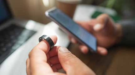 Nahaufnahme einer Hand, die einen Fitnessring hält, während in der anderen Hand ein Smartphone zu sehen ist