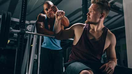Zwei trainierte Männer im Fitnessstudio bei der Langhantelstation geben sich die Faust