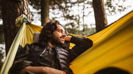 Mann liegt in gelber Hängematte im Wald