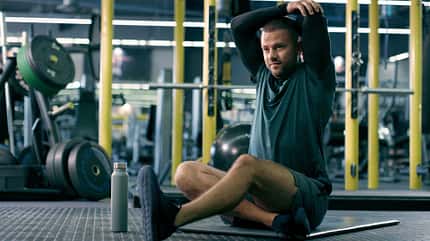 Mann sitzt auf einer Matte im Fitnessstudio und dehnt die Schultern nach dem Training. Mann sitzt auf einer Matte im Fitnessstudio und dehnt die Schultern nach dem Training.