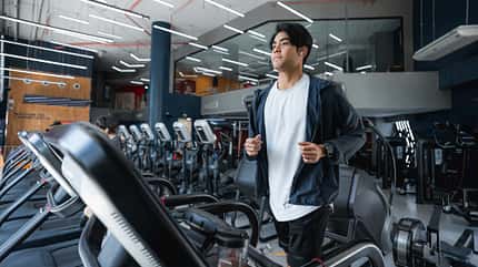 Mann läuft auf einem Laufband im Fitnessstudio, mit Kopfhörern im Ohr