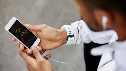 Person mit Kopfhörern schaut auf ein Smartphone mit aufgezeichneter Laufroute und Trainingsdaten.