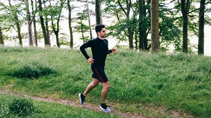 Ein Mann joggt in Laufkleidung einen Waldweg entlang