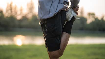 Ein Mann steht in der Natur und dehnt sein linkes Bein