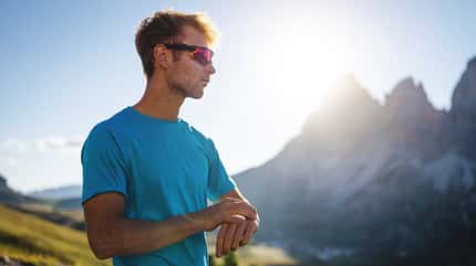 Ein junger Mann mit Sportbrille steht in den Bergen