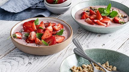 Mehrere Schalen mit Erdbeeren, Joghurt und Mandeln stehen auf einem Holztisch