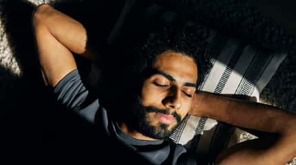 Ein Mann liegt mit seinen Armen hinter seinem Kopf verschränkt in der Sonne