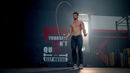 Sportlicher Mann springt in einem dunklen, leeren Gym Springseil Sportlicher Mann springt in einem dunklen, leeren Gym Springseil