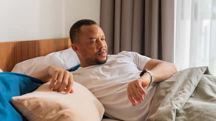 Ein Mann liegt im Bett und schaut auf seine Fitnessuhr