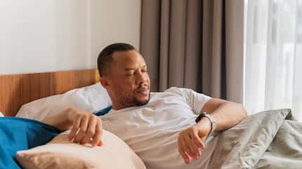 Mann im Bett prüft Gesundheitsdaten auf dem Smartphone