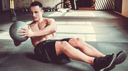 Ein Mann mit definiertem Sixpack führt Russian Twists aus mit einem Medizinball