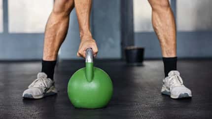 Ein männlicher Sportler, der während einer Krafttrainingsübung eine grüne Kettlebell festhält