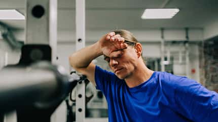 Mann lehnt sich müde an ein Fitnessgerät an Mann lehnt sich müde an ein Fitnessgerät an