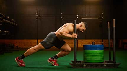 Ein Sportler stemmt sich gegen einen Schlitten im Fitnessstudio Ein Sportler stemmt sich gegen einen Schlitten im Fitnessstudio
