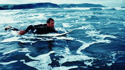 Surfer im Neoprenanzug paddelt auf seinem Surfbrett raus hinter die Wellen