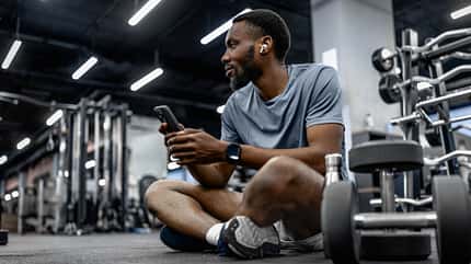 Ein Mann sitzt im Gym beim Training und schaut auf sein Smartphone