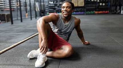 Ein junger Mann sitzt im Fitnessstudio lachend auf dem Boden