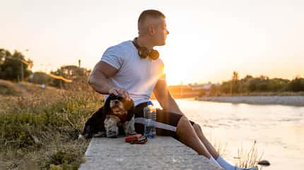 Ein muskulöser Mann sitzt mit seinem Hund am Wasser Ein muskulöser Mann sitzt mit seinem Hund am Wasser