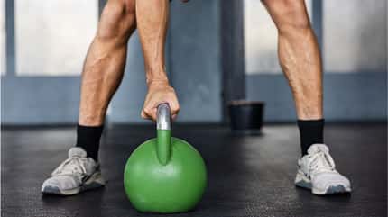Close-Up zweier männlicher Beine und einem muskulösen Arm der eine Kettlebell hält. Close-Up zweier männlicher Beine und einem muskulösen Arm der eine Kettlebell hält.