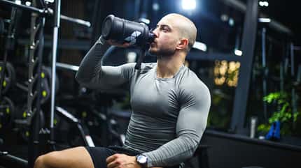 Ein muskulöser Sportler sitzt auf einer Bank im Fitnessstudio und trinkt einen Protein-Shake. Ein muskulöser Sportler sitzt auf einer Bank im Fitnessstudio und trinkt einen Protein-Shake.