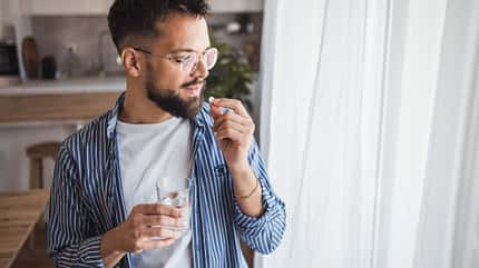 Mann steht am Fenster und nimmt eine Tablette ein