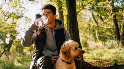 Mann macht mit seinem Hund im Wald eine Trinkpause