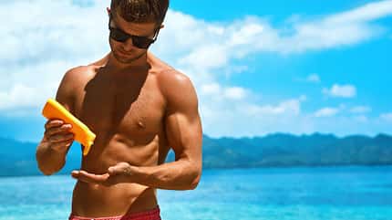 Mann cremt sich am Strand mit Sonnenschutz ein Mann cremt sich am Strand mit Sonnenschutz ein