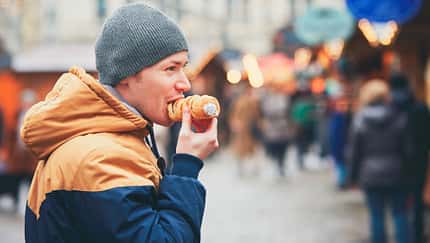 Mann mit Mütze isst auf dem Weihnachtsmarkt eine süße gefüllte Blätterteigrolle