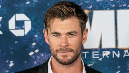 Chris Hemsworth trägt ein Jacket und ein offenes Hemd bei einer Präsentation eines Films.