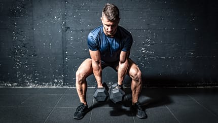 Mann hält im Squat zwei schwere Kurzhanteln und ist im Begriff, sie hochzustemmen