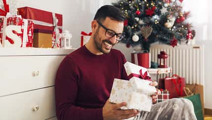 Smiling,Young,Man,Opening,Christmas,Gift,At,Home