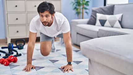 Mann macht im Wohnzimmer Fitnessübungen.