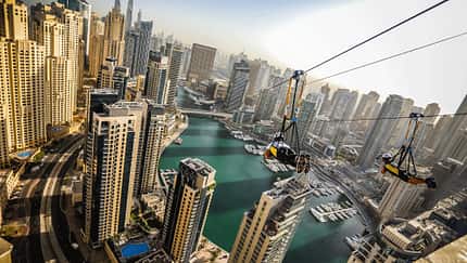 Man sieht eine Zipline über der Marina von Dubai an der eine Person hängt: Die Zipline ist über einen Kilometer langen und befindet 170 Meter über dem Erdboden