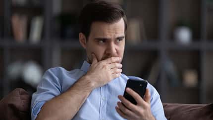 zweifelhafter Mann sitzt auf dem Sofa und schaut von seinem Smartphone auf