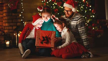 Familie schaut in ein Geschenk unter dem Tannenbaum.