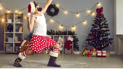 Ein Mann tanzt als Weihnachtsmann verkleidet um den Christbaum