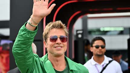Brad Pitt hebt die Hand und lächelt in die Kamera