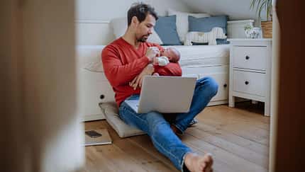 Frischgebackener Vater gibt seinem Nachwuchs das Fläschchen während er am Notebook sitzt