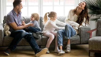 Mutter und Vater sitzen mit ihren zwei Kindern auf dem Sofa und albern herum