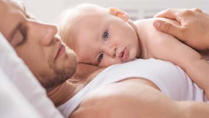 Ein Vater liegt im Bett und hat sein Baby auf der Brust