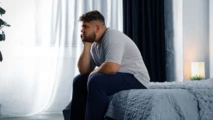 Mann sitzt betrübt auf dem Bett 