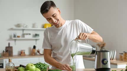 Junger Mann bereitet grünen Smoothie zu
