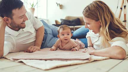 Mutter und Vater liegen mit ihrem neugeborenen Kind auf dem Fußboden auf einer Babydecke