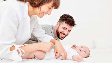 Ein Vater schaut der Mutter dabei zu, wie sie ihr Baby wickelt