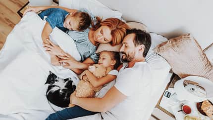 Vater, Mutter, zwei Kinder und eine Katze liegen alle zusammen in einem großen Bett und schlafen zufrieden
