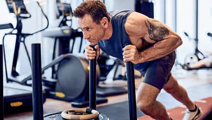 Superstar Jason Fox schiebt einen Gewichtsschlitten im Gym.
