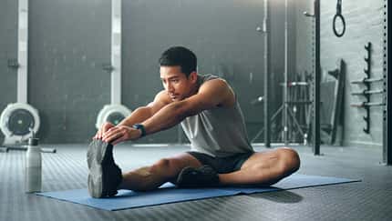 Mann stretcht sich sitzend im Gym