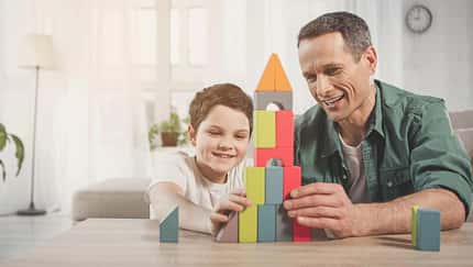 Ein Vater sitzt am Tisch und spielt mit seinem Sohn mit Bauklötzen